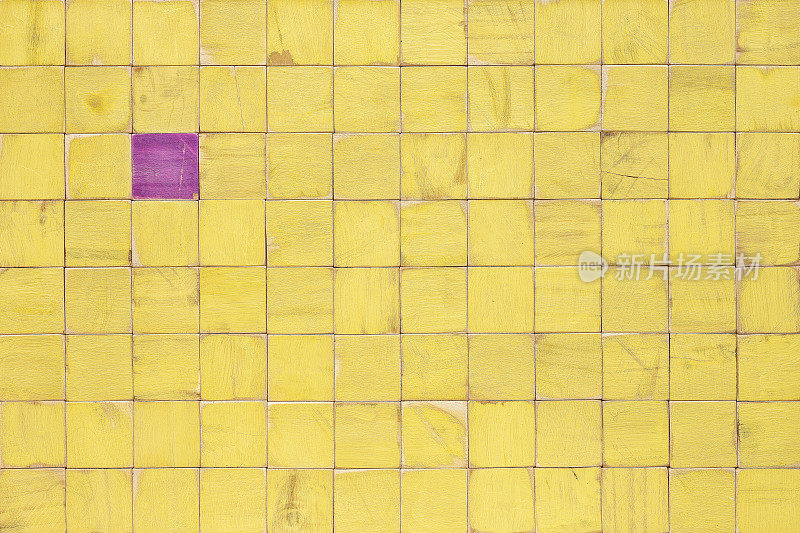 许多稻草黄色的木块或带有木质纹理的侧面，与一个相对的紫色木块形成对比，坐在许多橙色的块中。