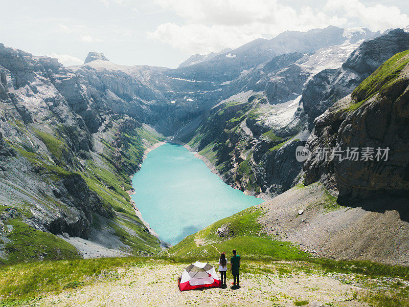 鸟瞰图两个徒步旅行者遇见风景优美的夏天日出的湖和山附近的帐篷在瑞士