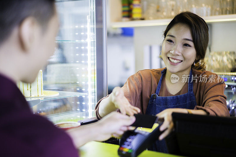 美丽的亚洲女招待收到信用卡无线支付客户在café。