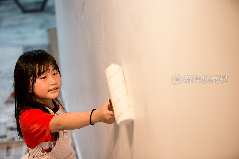 一个亚洲女孩正在用油漆滚筒帮助家庭粉刷他们的新房子