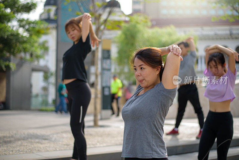 一个亚洲女人和她的朋友在运动服装热身和伸展在户外人行道上锻炼