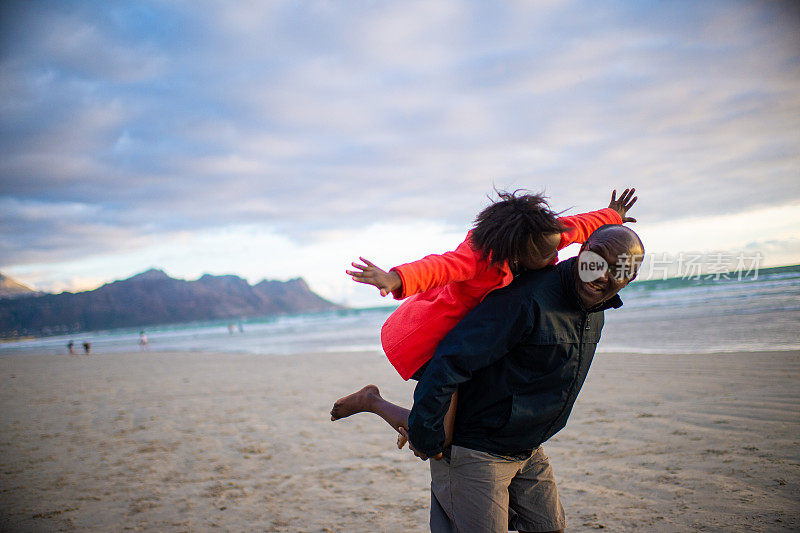 骑在背上的父亲和女儿在海滩上互相看着