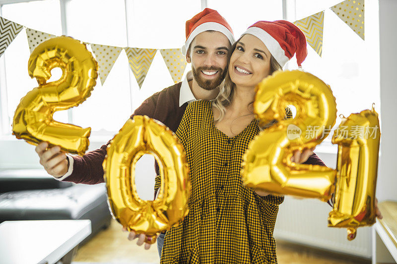 年轻夫妇在家庆祝新年，手持数字为2021的气球，代表即将到来的新年