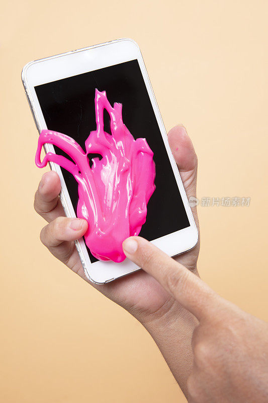 女人的手用智能手机与霓虹粉色黏液玩具在橙色波普艺术背景。