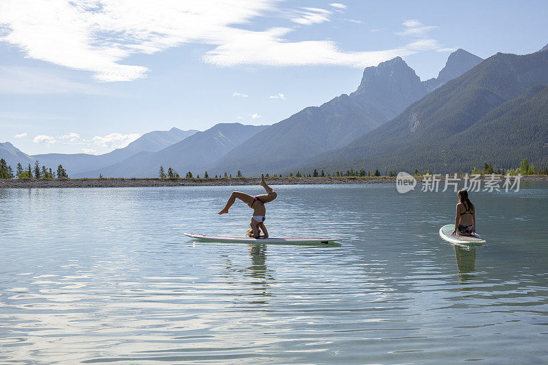 朋友们早上在高山湖上的冲浪板上练习瑜伽