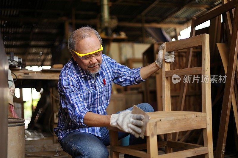 亚洲资深木匠正在他自己的车库风格的车间修理木椅在退休年龄的爱好