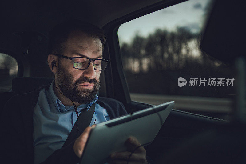 商人在汽车上使用平板电脑。一个商人坐在一辆豪华轿车的后座上，这是一次商务旅行