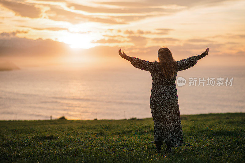 夕阳西下时举起双手的年轻女子