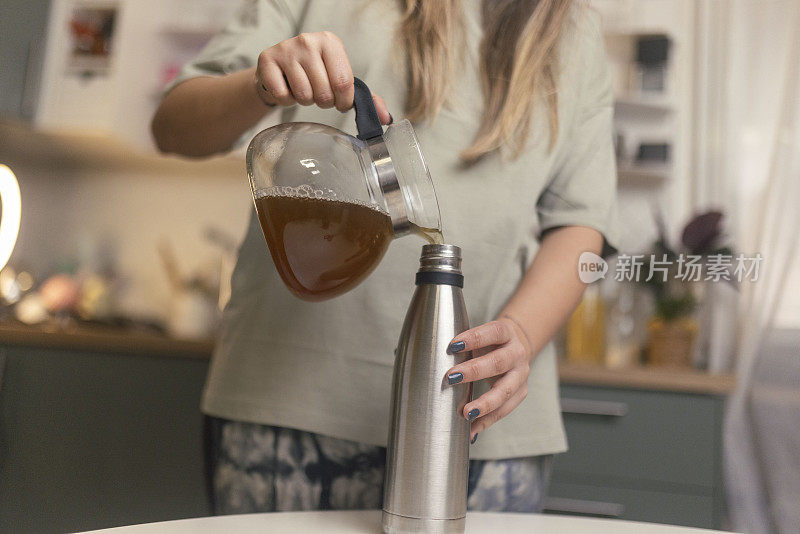 为了保持茶的热度，这位女士把茶壶里的茶倒进厨房里一个可重复使用的瓶子里