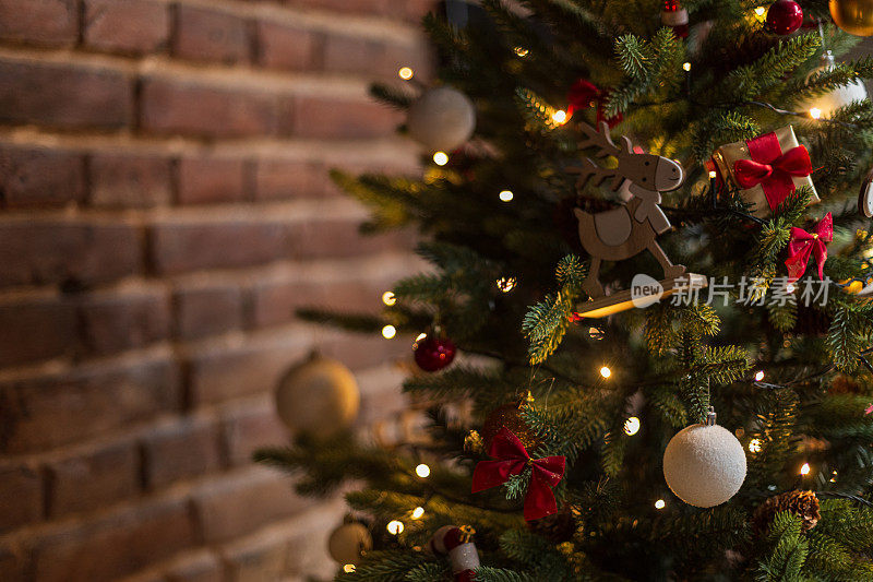 美丽的圣诞树，在圣诞前夜的砖墙旁，挂着木制鹿、礼物、球和灯的复古玩具。新年贺卡