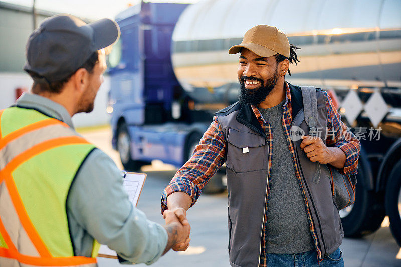 快乐的黑人卡车司机和货运经理在停车场握手。