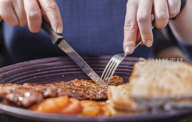 餐桌礼仪:女人用手拿刀叉切盘子里的肉。