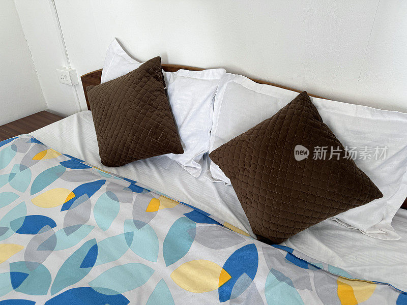 木制床头板的双人床的特写图像，复古风格的棕色绗缝靠垫叠在白色枕头上，有图案的被套，木制床头柜，重点放在前景上，抬高视野