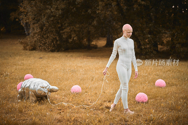 在秋天的公园里，穿着白布的秃头小女孩走着缓步动物玩具的肖像