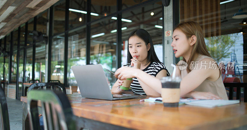 两名年轻女子坐在咖啡店里用笔记本电脑开会。