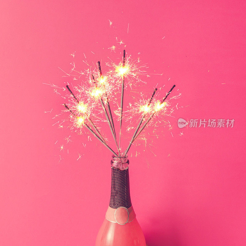 粉色背景上有火花的香槟瓶。平的。