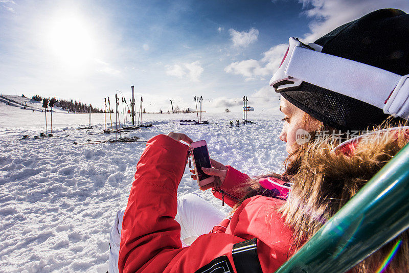 一个年轻女子在滑雪胜地用手机发短信。