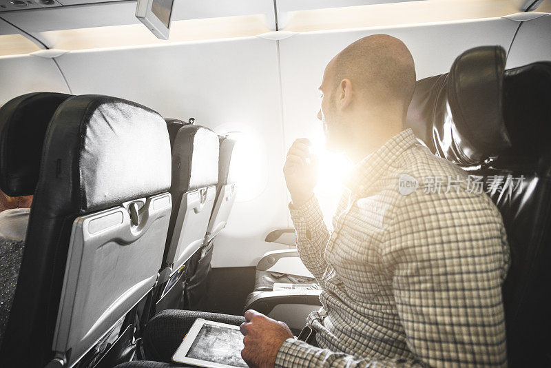 沉思的商人在飞机上用数字平板电脑工作