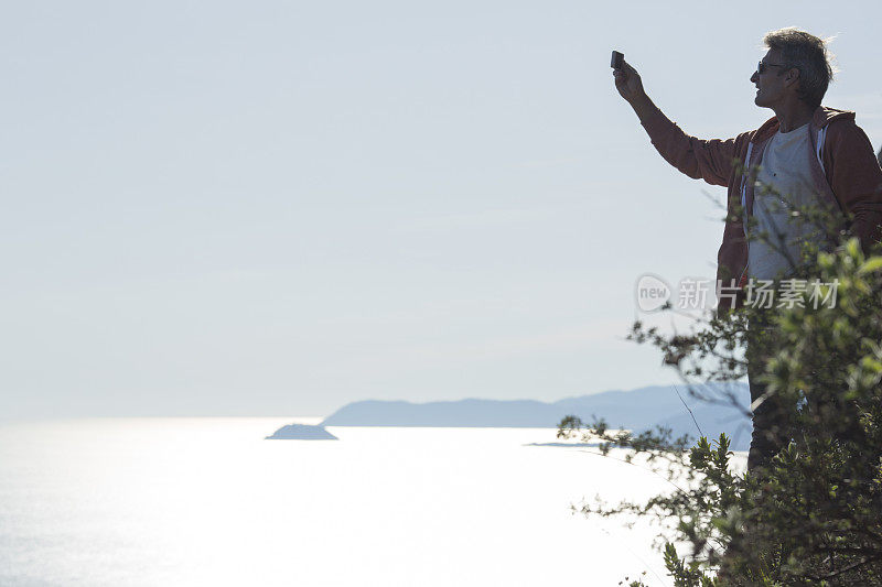 一名男子在海对面茂密的小丘上拍照