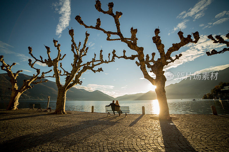 日落时分，人们坐在湖边的长凳上