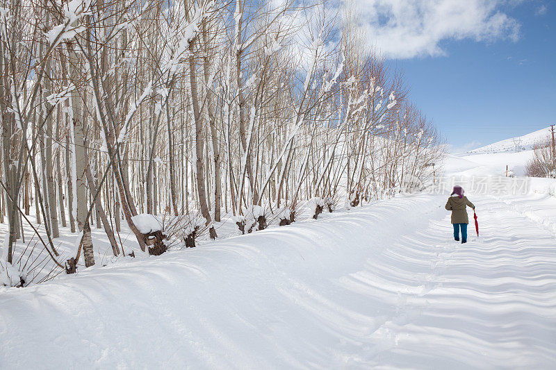 女人撑着红伞走在雪道上