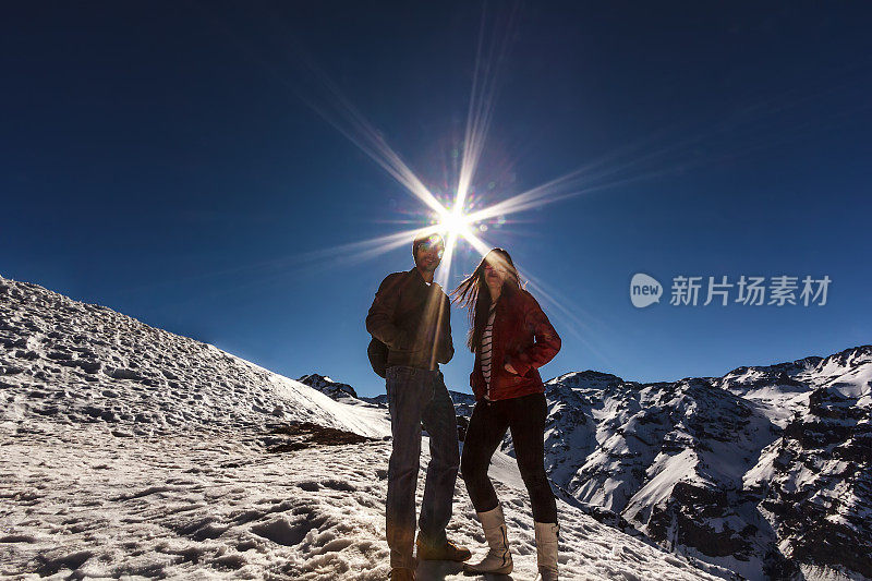 一对情侣站在雪山上，在耀眼的太阳下