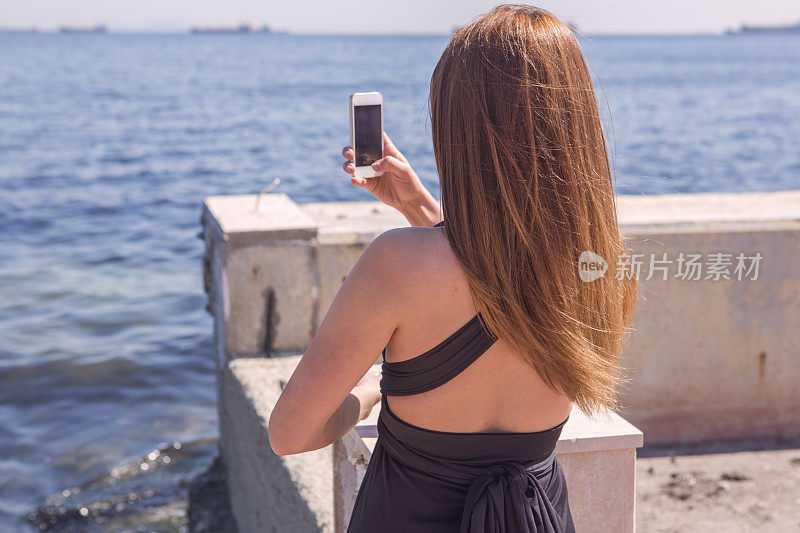 在土耳其伊斯坦布尔马拉马拉海岸用智能手机拍照的年轻女性
