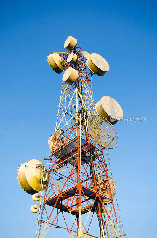 电信塔在蓝天上，一红一白，另一白，天线用于电视、收音机和移动电话。