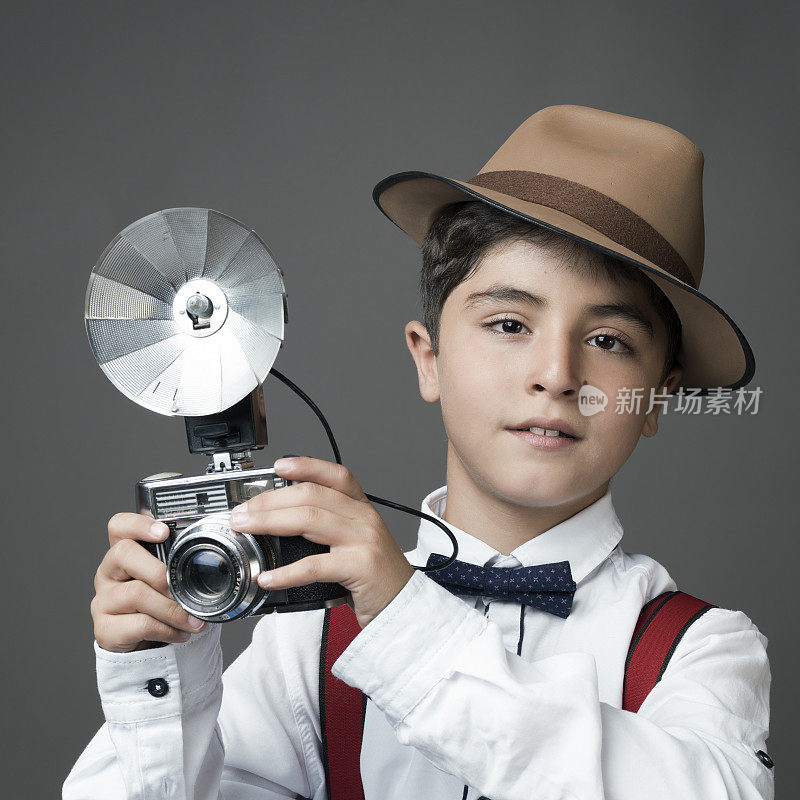 小男孩戴着软呢帽，拿着老式相机