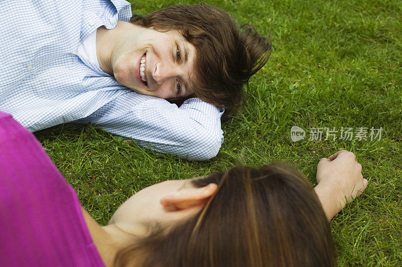 一对年轻夫妇躺在草地上，面带微笑