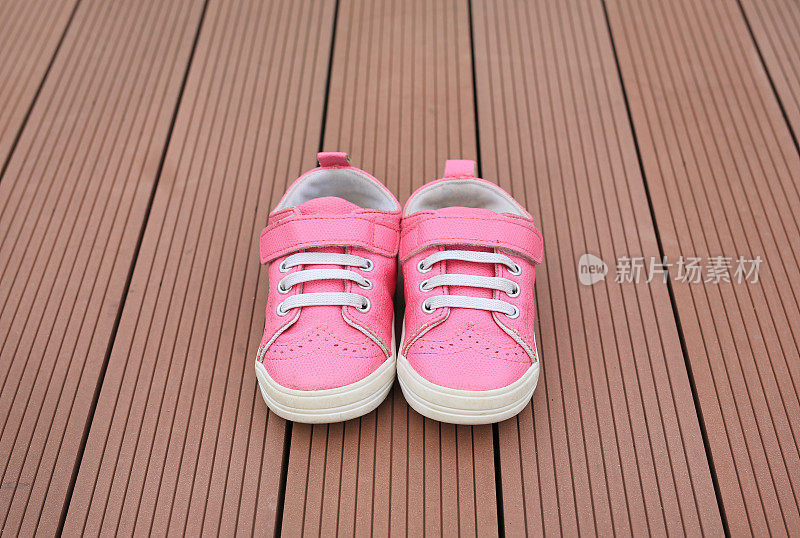 一双粉红色的婴儿皮革运动鞋在木板的背景。