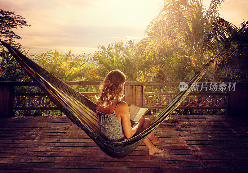 日落时分，在丛林的吊床上，一个穿着礼服的女人在看书。