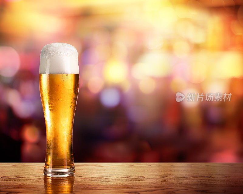 金色的啤酒在玻璃与酒吧的灯光在背景
