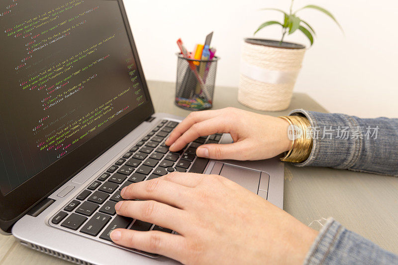 编程工作时间。程序员输入新的HTML代码行。笔记本电脑和手特写。工作时间。网站设计的商业概念。