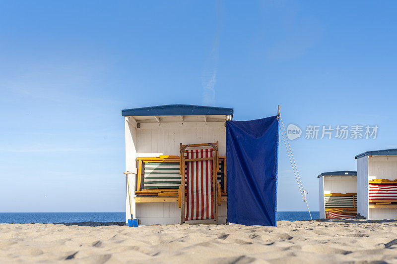 在晴朗的日子里，荷兰北海海岸上五颜六色的空海滩小屋配有沙滩椅和挡风玻璃。这张图片有GPS标记