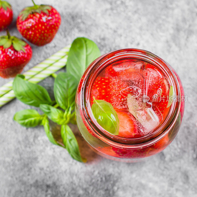 俯视图的夏季食物和饮料。水泥桌上放着一瓶草莓罗勒柠檬水。复制空间，方形图像