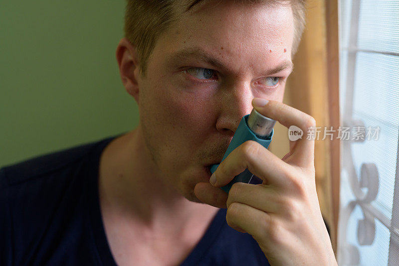 年轻英俊的男子在家里使用哮喘吸入器的肖像