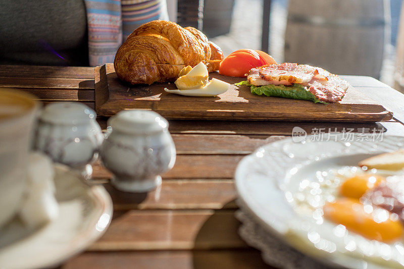 早餐有鸡蛋，熏肉，牛角面包和西红柿在木托盘上，俯瞰