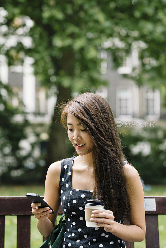 年轻的亚洲学生在伦敦公园检查电话