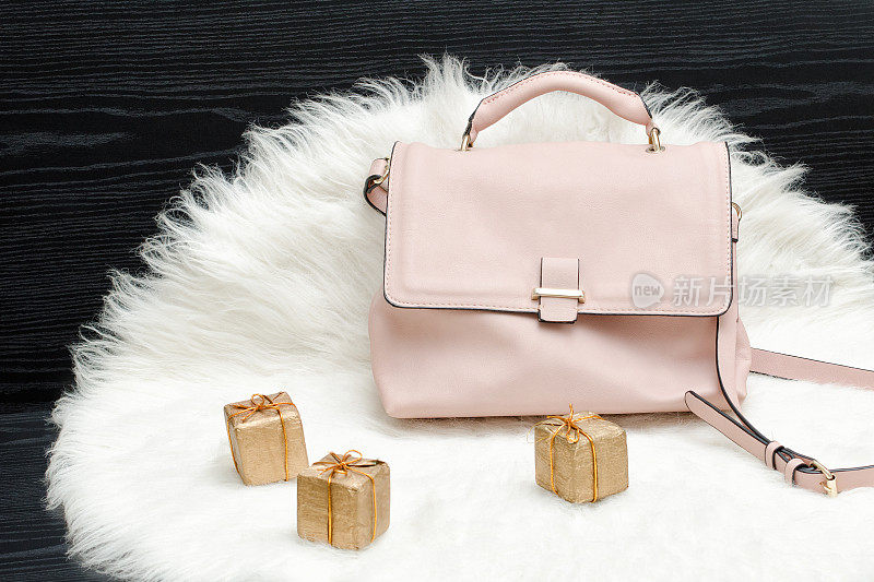 粉色的包和礼盒，白色的皮毛，黑色的桌子。时尚的概念