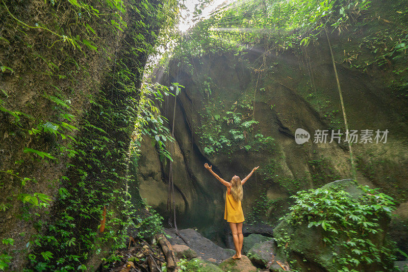 在巴厘岛的热带雨林中，旅行的年轻女子张开双臂拥抱大自然的美丽。人们以自然为旅游理念。