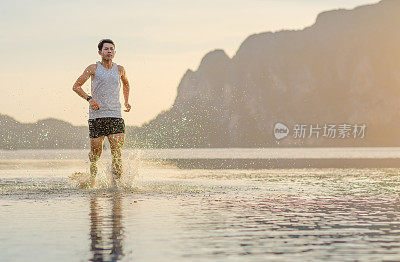 年轻的亚洲男子在海滩上奔跑，夕阳为背景