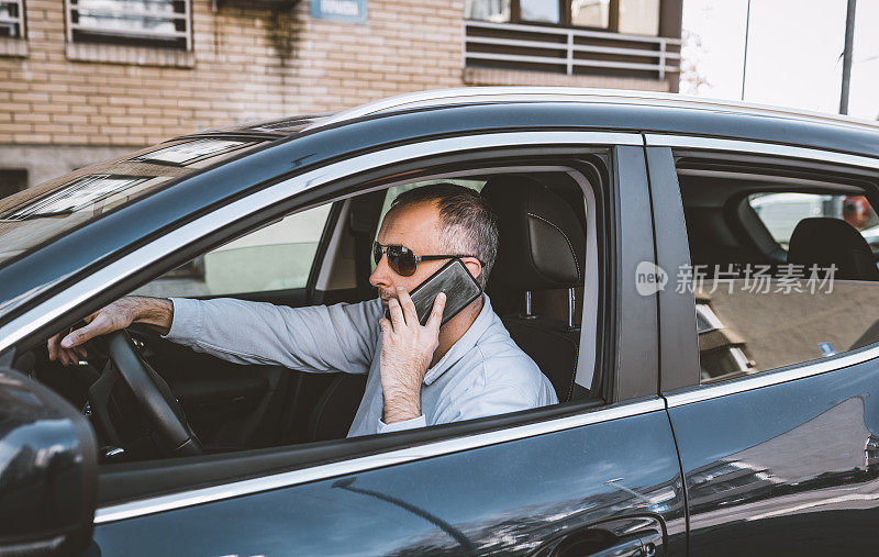 一个英俊的男人一边开车一边用手机。