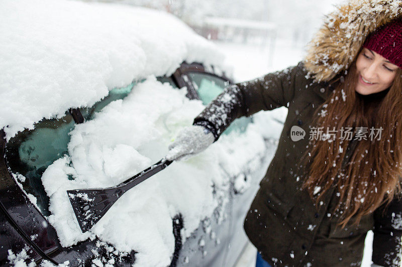 年轻女子在清理车上的积雪