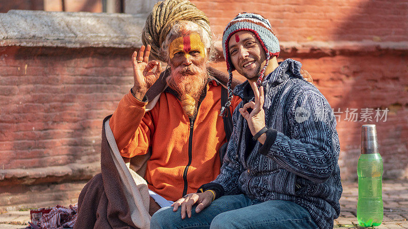 一名戴帽子的男子和神职人员坐在pashupatinath神庙里