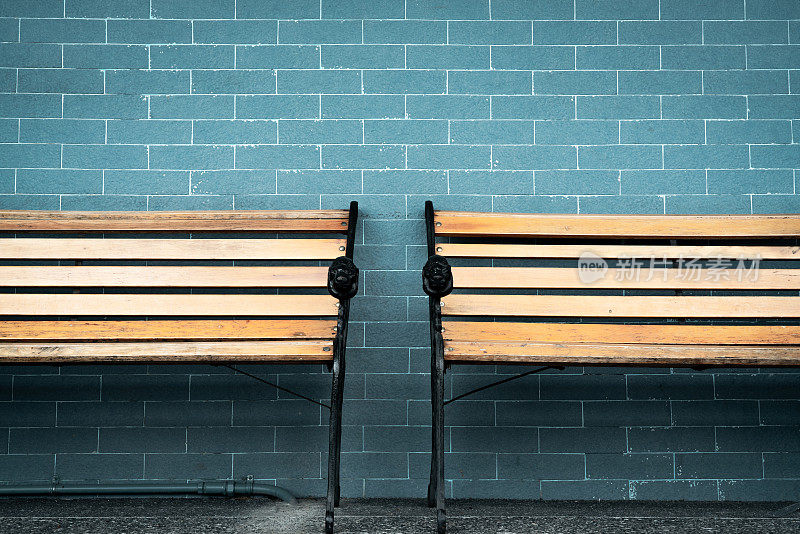 两个空木凳在绿色砖墙的背景上。等着有人来填满空木椅。建筑外的棕色木凳。等概念。空墙与空间报价。