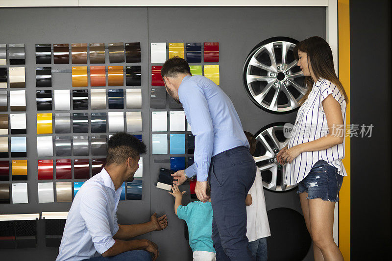 新车推销员帮助一对夫妇和孩子们选择一个完美的颜色为他们的新车在汽车经销商