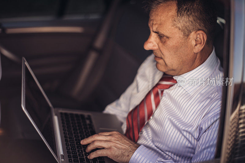 一个商人开车时在汽车后座上使用笔记本电脑