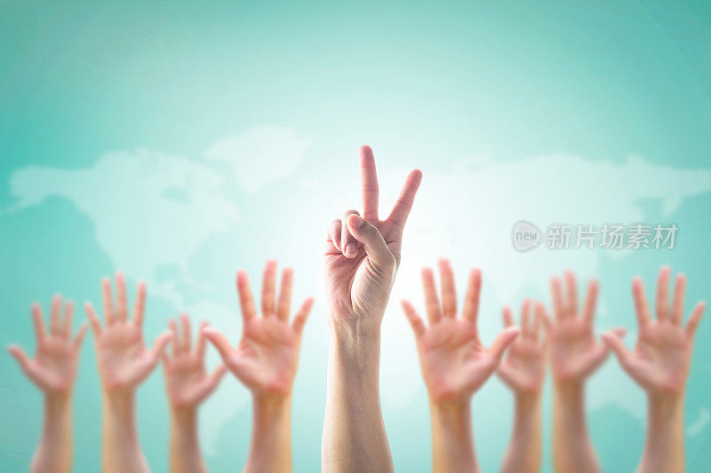 模糊的双手中领袖的两个手指胜利手势人群:许多人模糊的手掌向上在复古的蓝天背景地图:世界参与，领导志愿者的概念:V日