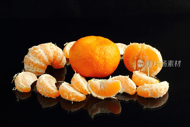新鲜的带叶子的橘子去皮，放在黑色的石头表面上。附近的华语片。季节性柑橘类水果，天然健康食品。特写镜头。黑石的背景。Copyspace文本。